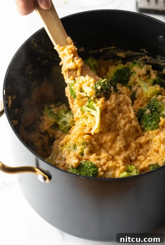Spoon stirring mixture of rice, broccoli, and cheese in a pot.