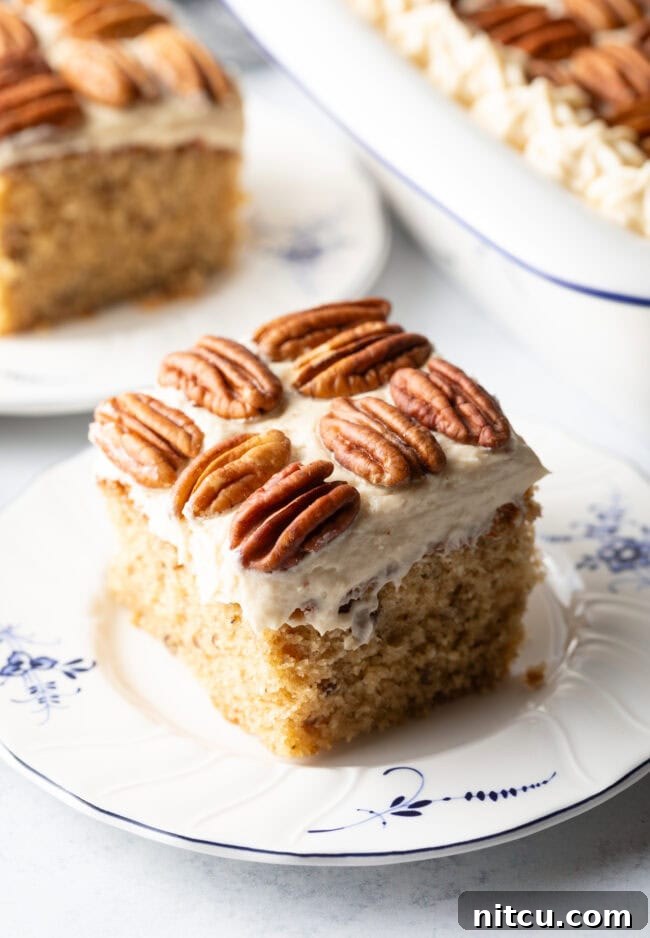 Square of brown butter cake on a plate with pecan halves on top of the white frosted cake.