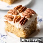 Square of brown butter cake on a plate with pecan halves on top of the white frosted cake.