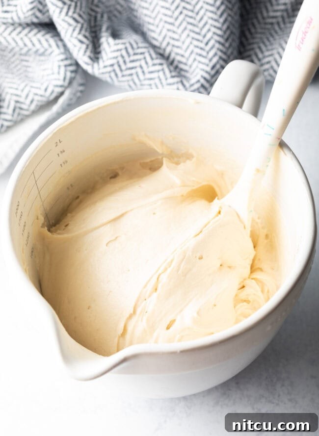 Homemade white frosting in a white mixing bowl with spatula.