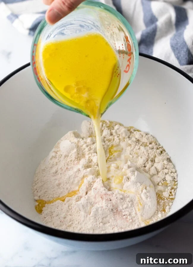 Adding melted butter to the flour mixture in a large white mixing bowl, a step in making unleavened bread.