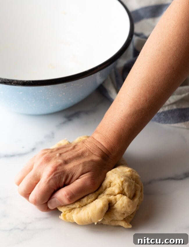 A hand kneading a ball of unleavened bread dough to achieve a smooth consistency.
