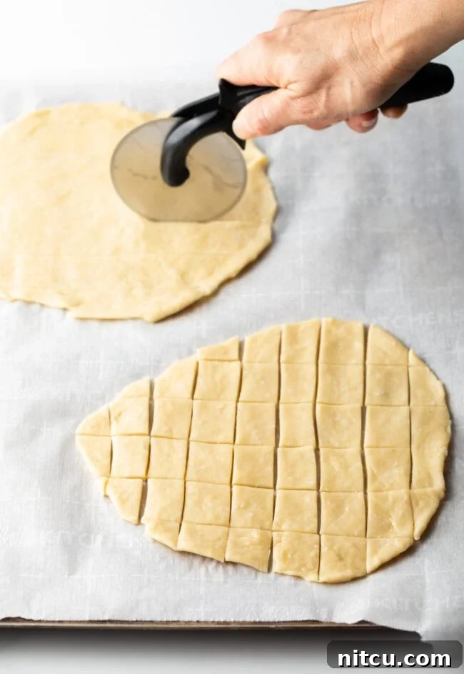 A hand using a pizza cutter to slice two unbaked ovals of unleavened bread into tiny squares for communion.