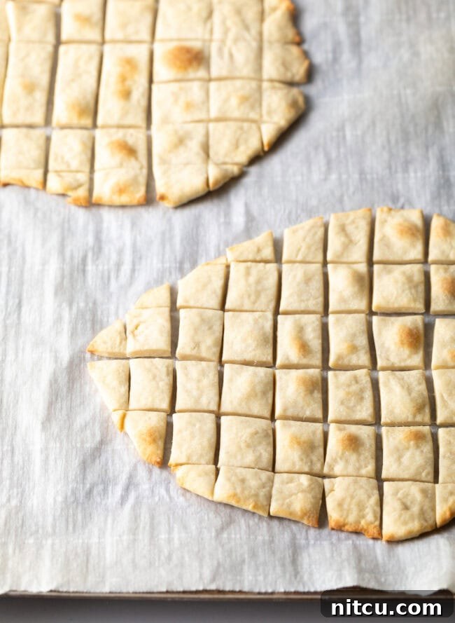 Two pieces of unleavened bread laying on a gray background. Each large oval of bread has been sliced into small squares, ready for communion.