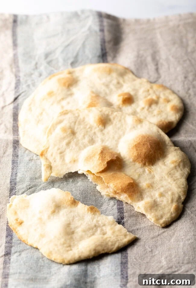 Two pieces of unleavened bread laying on a gray background, one of which has been gently split to reveal its soft interior.