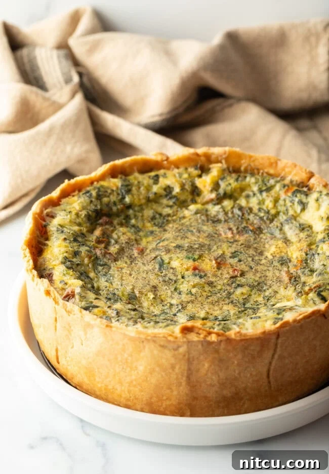 Baked veggie quiche with a golden deep dish crust on a white round plate, ready to be served.