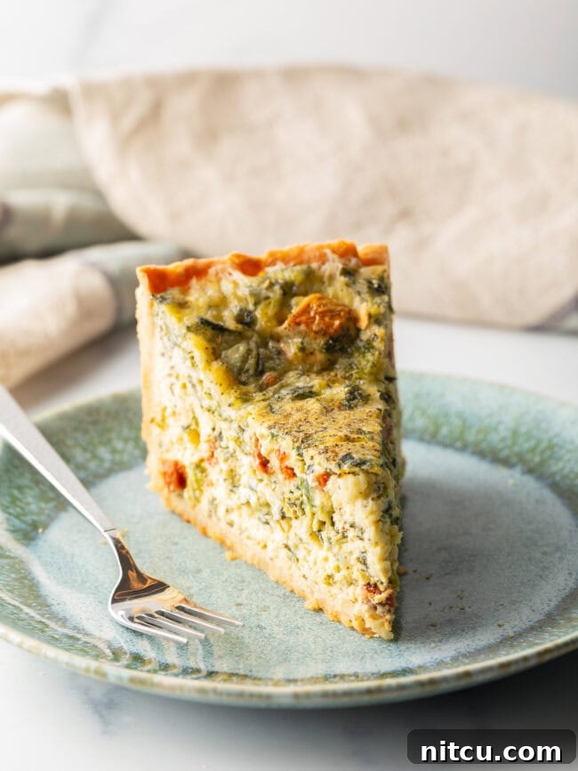 A delectable slice of quiche, tall and inviting, rests on a light blue plate, accompanied by a fork, ready for enjoyment.