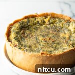 Baked veggie quiche with a deep dish crush on a white round plate.