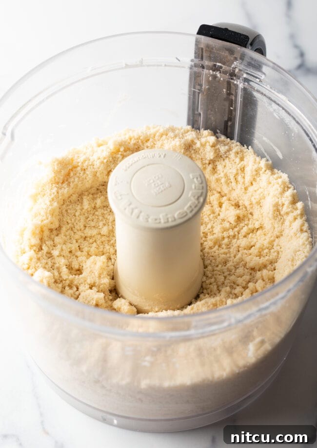 Crumbly pie dough ingredients within a food processor, before being fully combined, illustrating the ideal texture for starting the shortcrust.
