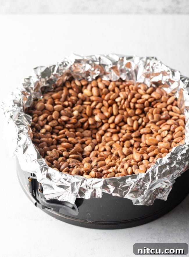 A pie crust being blind-baked in a springform pan, lined with aluminum foil and filled with dry kidney beans to hold its shape.
