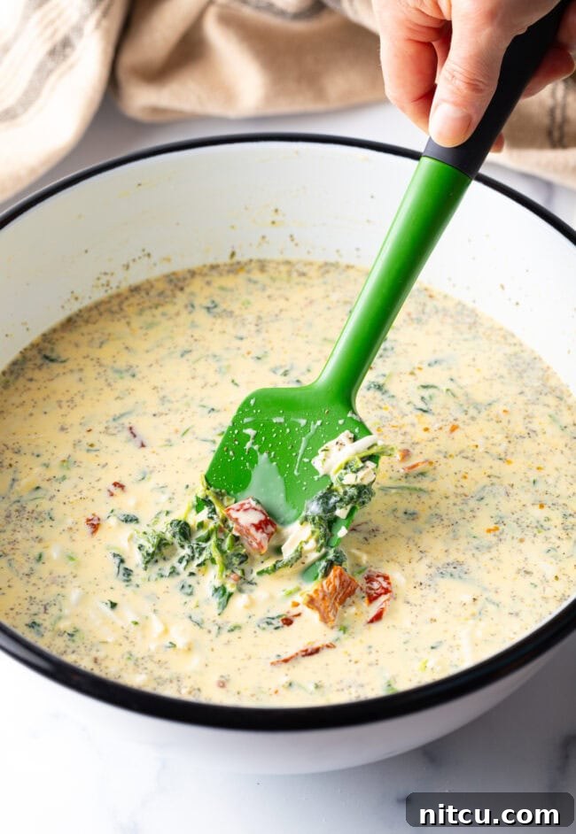 A white mixing bowl filled with the vibrant egg and veggie quiche filling, being stirred with a green spatula, showing the rich texture before baking.