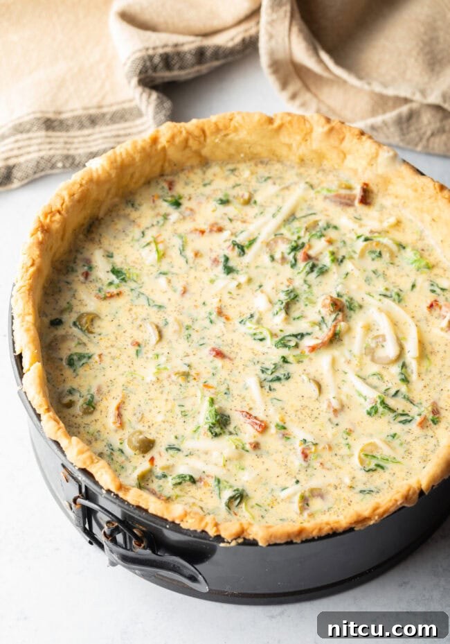Top-down view of the unbaked egg and vegetable mixture settled into a deep dish pie crust within a springform pan, ready for its final bake.