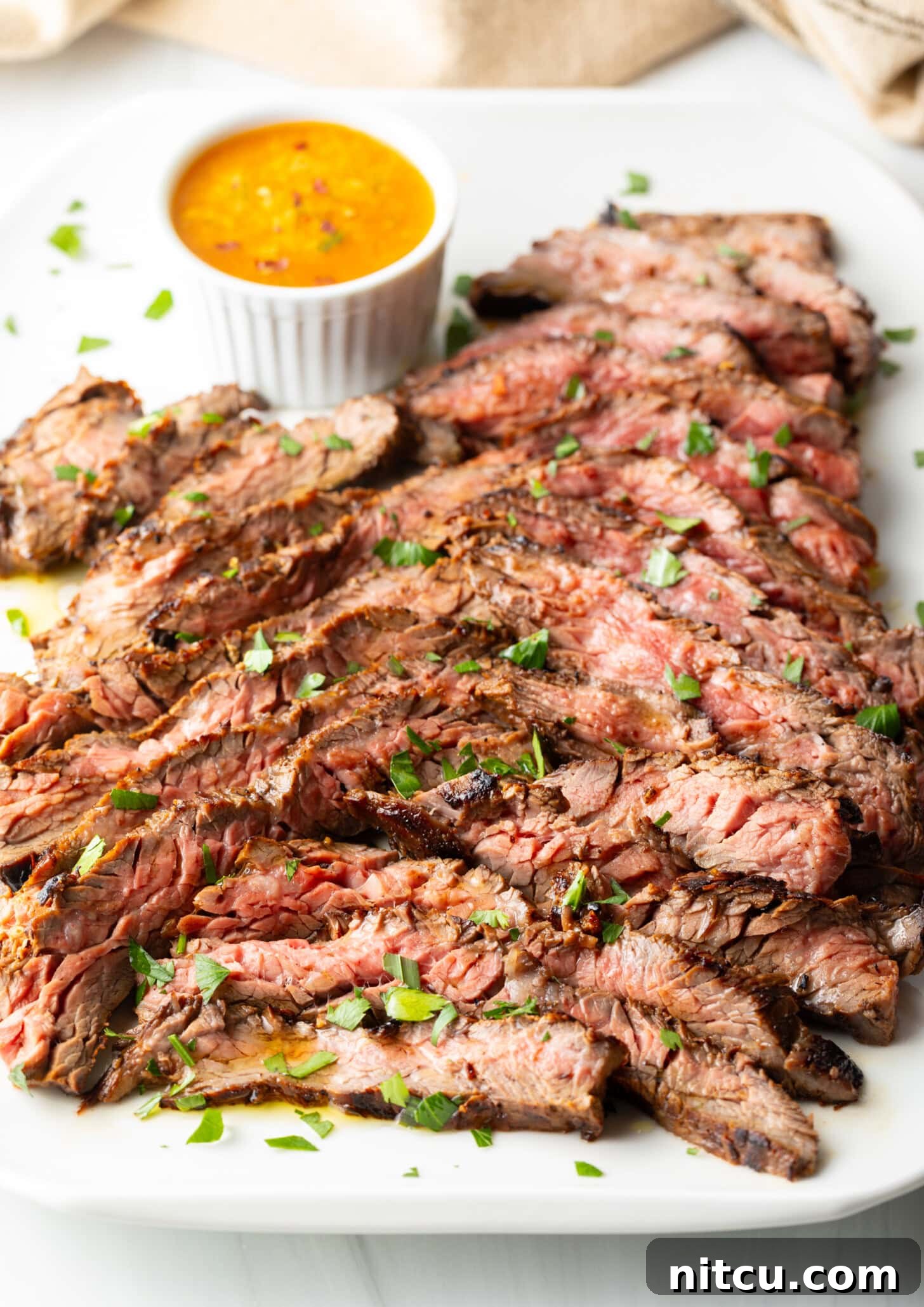 Thin slices of Bavette steak on a white serving platter with a ramekin of cowboy butter to the side.
