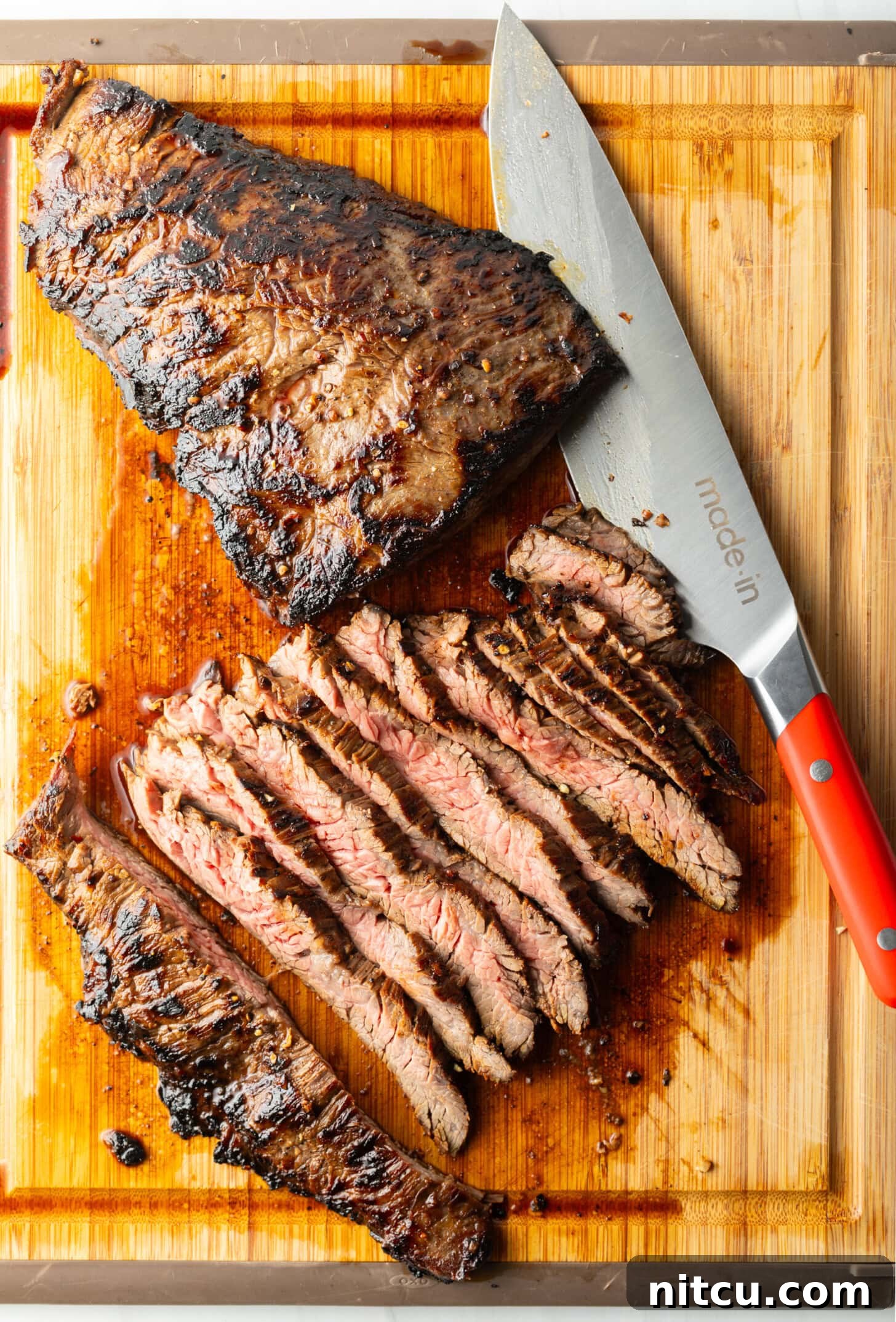 Seared steak sliced into thin strips on a wood cutting board, large knife to the side.