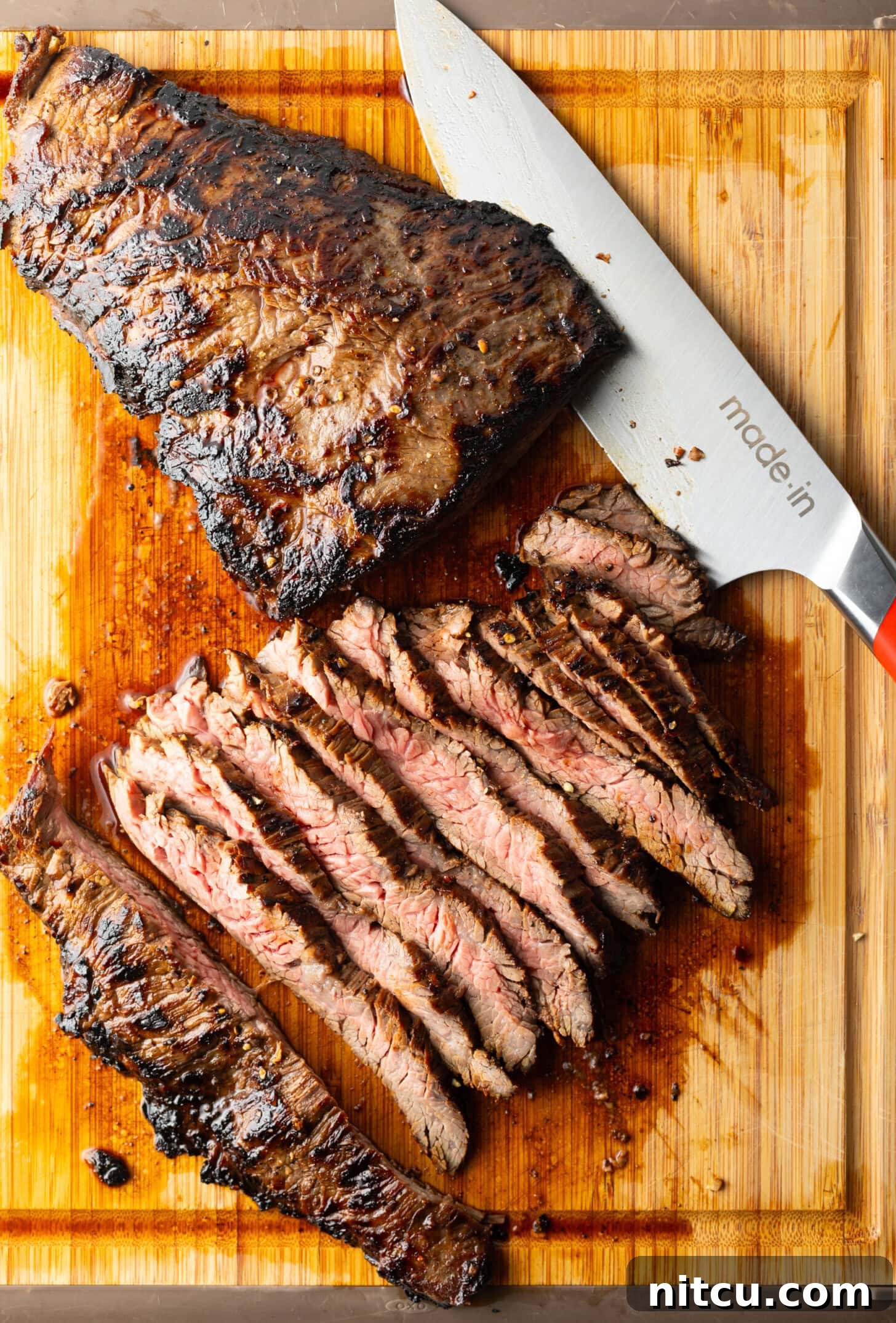 Seared steak sliced into thin strips on a wood cutting board, large knife to the side.