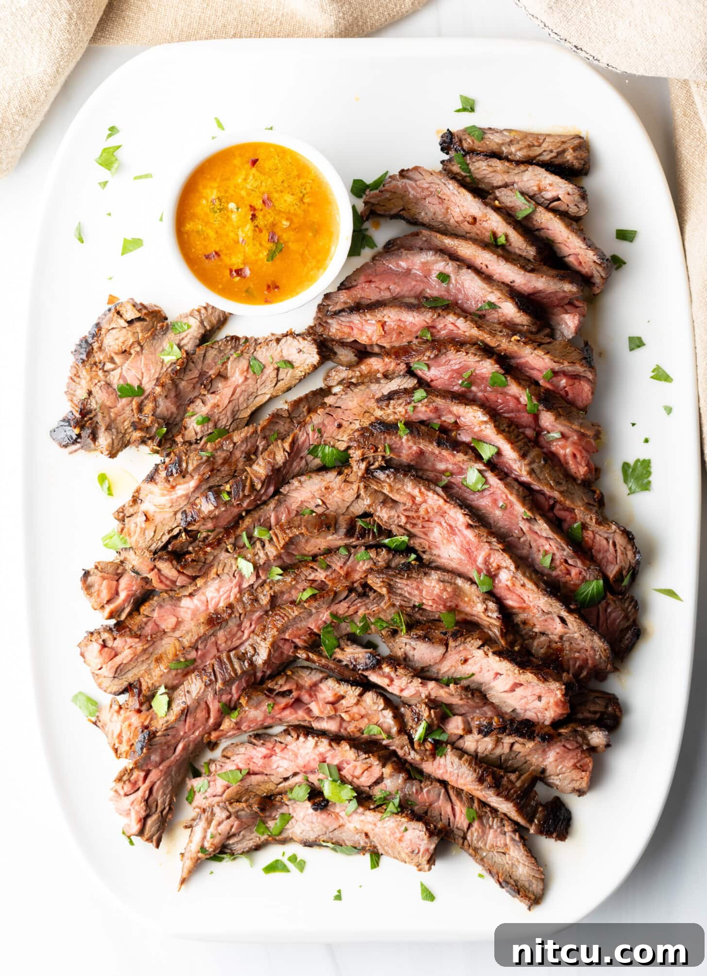 Thin slices of Bavette steak on a white serving platter with a ramekin of cowboy butter to the side.