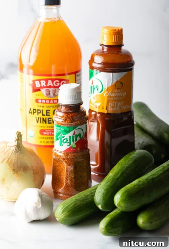 Recipe ingredients: Jars of apple cider vinegar, Tajin seasoning, and chamoy sauce. Also several small cucumbers, a whole onion, and head of garlic.