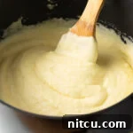 Creamy whipped potatoes in a black large pot, with a wooden spoon in the pot.