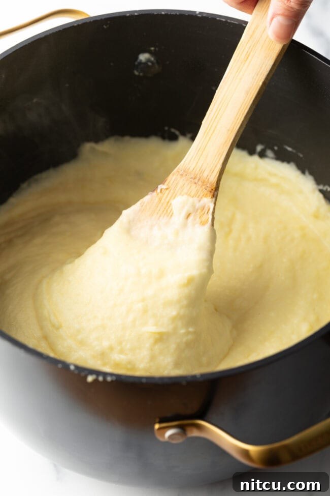 Creamy whipped potatoes in a black large pot, with a wooden spoon in the pot.