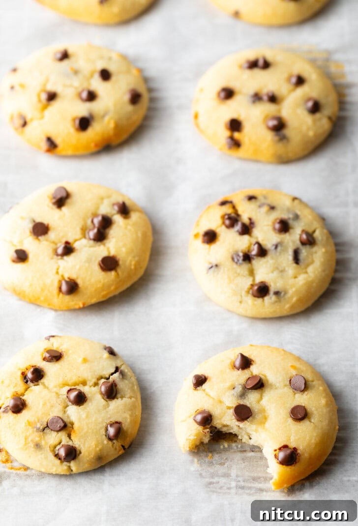8 cottage cheese chocolate chip cookies cooling on a baking sheet. A front cookie has a bite missing.