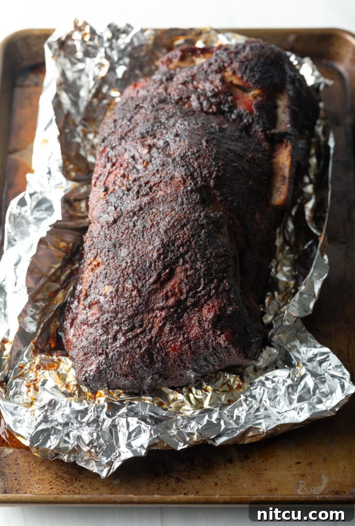 A beautifully smoked pork butt, just unwrapped from aluminum foil, revealing its dark, flavorful bark and tender exterior.