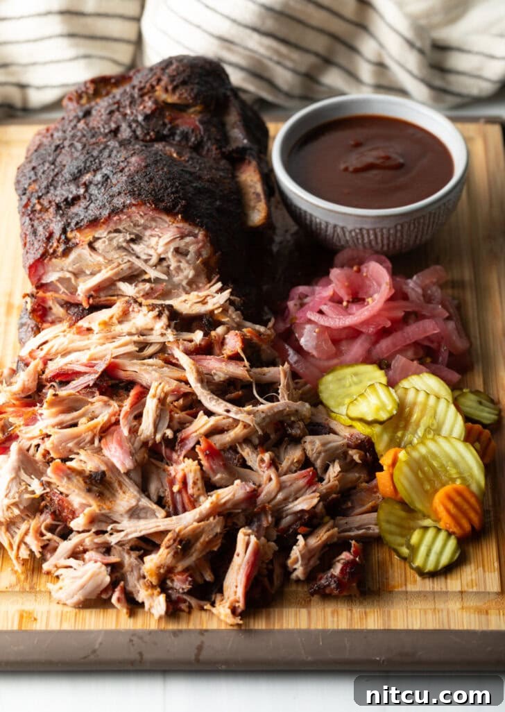 A close-up of the perfectly shredded smoked pork butt, glistening with juices, presented beautifully on a wooden cutting board with classic barbecue accompaniments.