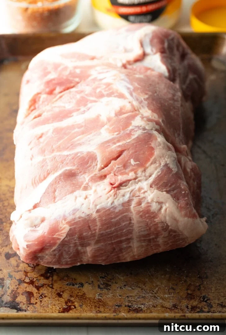 A large raw pork butt roast, glistening and ready for seasoning, sits on a cutting board.