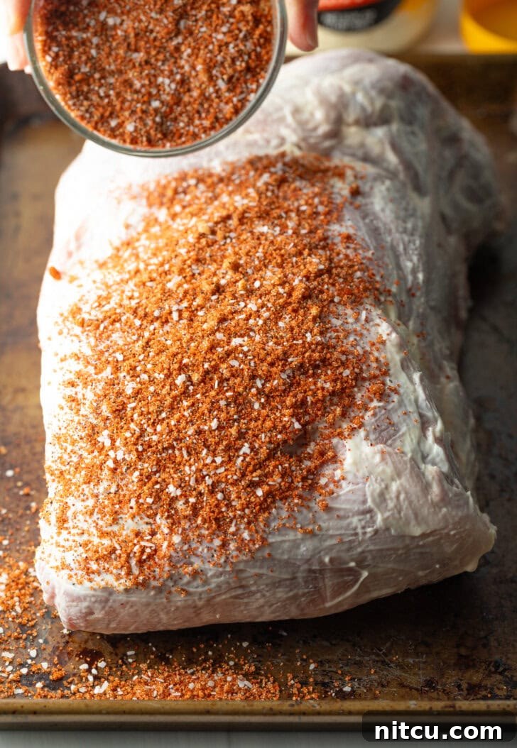 The raw pork shoulder generously covered in mayonnaise and then thoroughly seasoned with a thick layer of the dry spice rub, forming a flavorful crust.