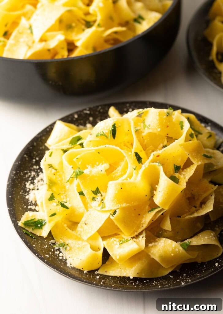 Top down view of a black bowl loaded with wide pappardelle pasta topped with fresh herbs and grated parmesan cheese.