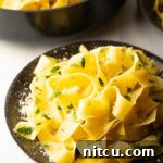 Top down view of a black bowl loaded with wide pappardelle pasta topped with fresh herbs and grated parmesan cheese.