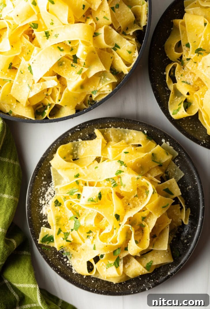 Top down view of a black bowl loaded with wide pappardelle pasta topped with fresh herbs and grated parmesan cheese.