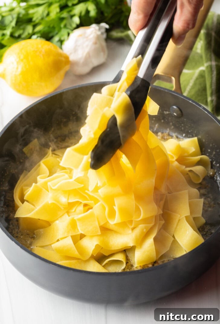 Tongs tossing pappardelle pasta with butter and garlic.