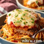 A cutlet of veal parmesan on top of spaghetti. A bite has been removed from the veal to show the juicy inside.
