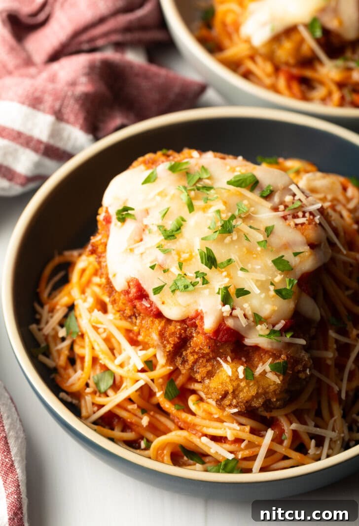 Breaded fried veal parmesan on top of spaghetti in a blue pasta bowl.