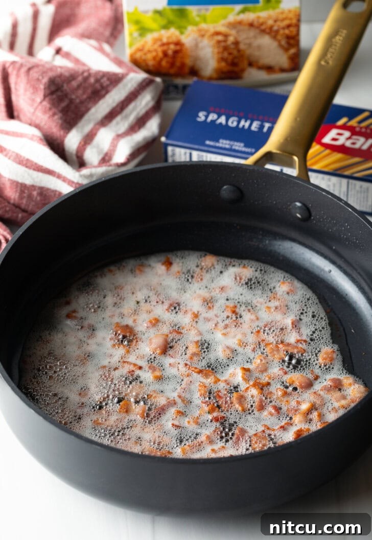 Cooking pieces of bacon in oil in a deep black skillet.