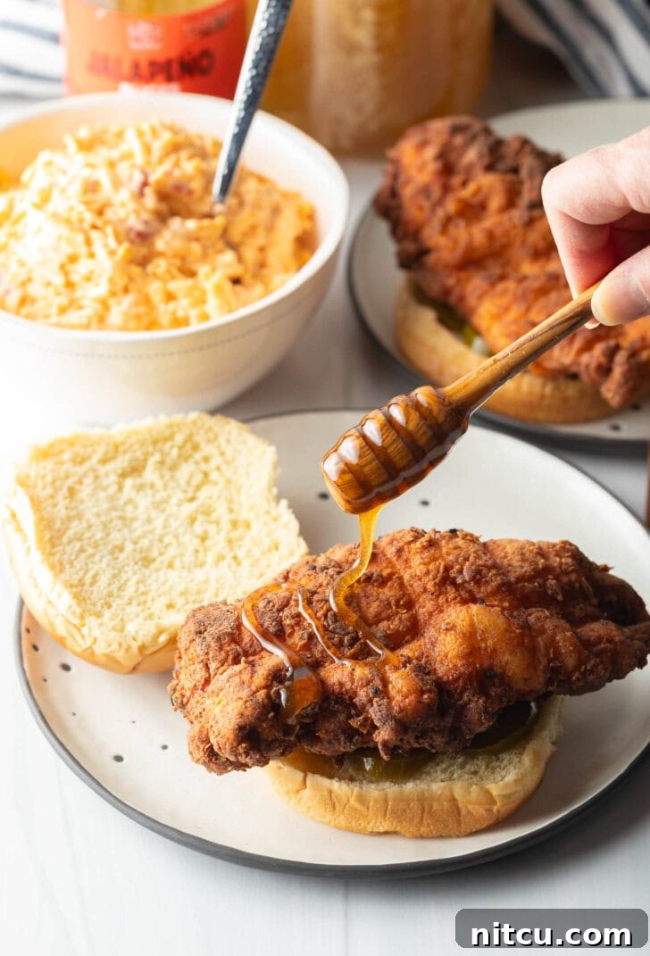 Drizzling honey onto a breaded chicken breast on the bottom half of a burger bun.