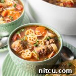 Green bowl of Italian meatball soup loaded with wheel shaped pasta, sliced carrots, in a tomato broth.