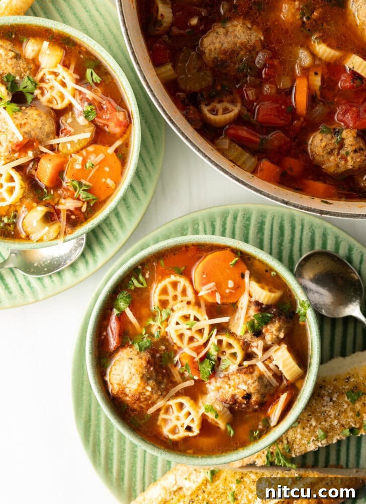 Top down two green bowls of Italian meatball soup loaded with wheel shaped pasta, sliced carrots, in a tomato broth.