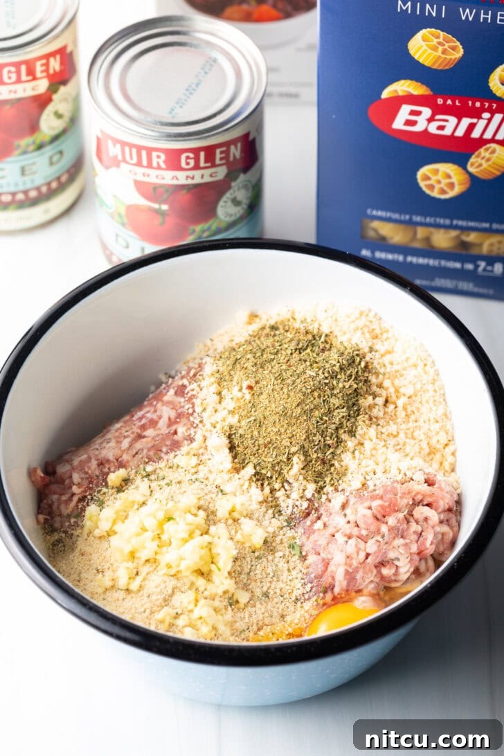 Meatball ingredients in a large white mixing bowl: ground sausage, breadcrumbs, diced onion, and spices.