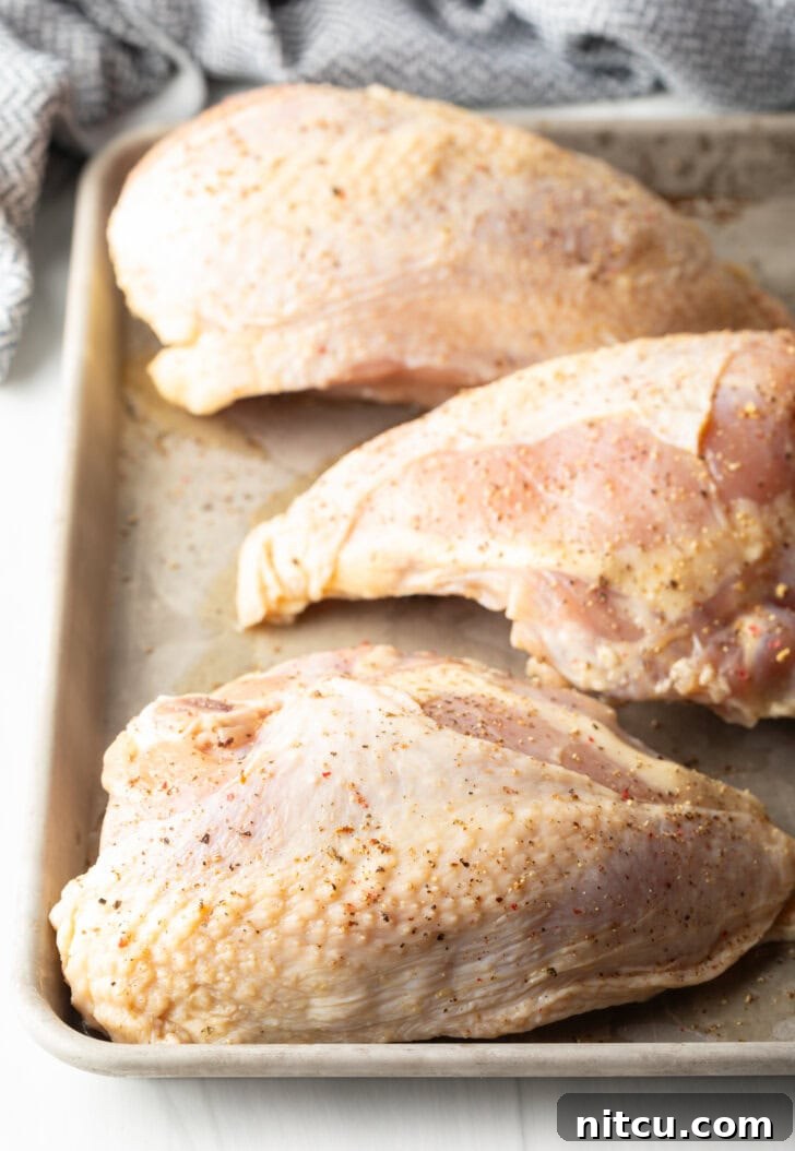 Three raw, skin-on chicken breasts arranged neatly on a baking sheet, impeccably prepared and ready for seasoning and cooking after their beneficial brining period.