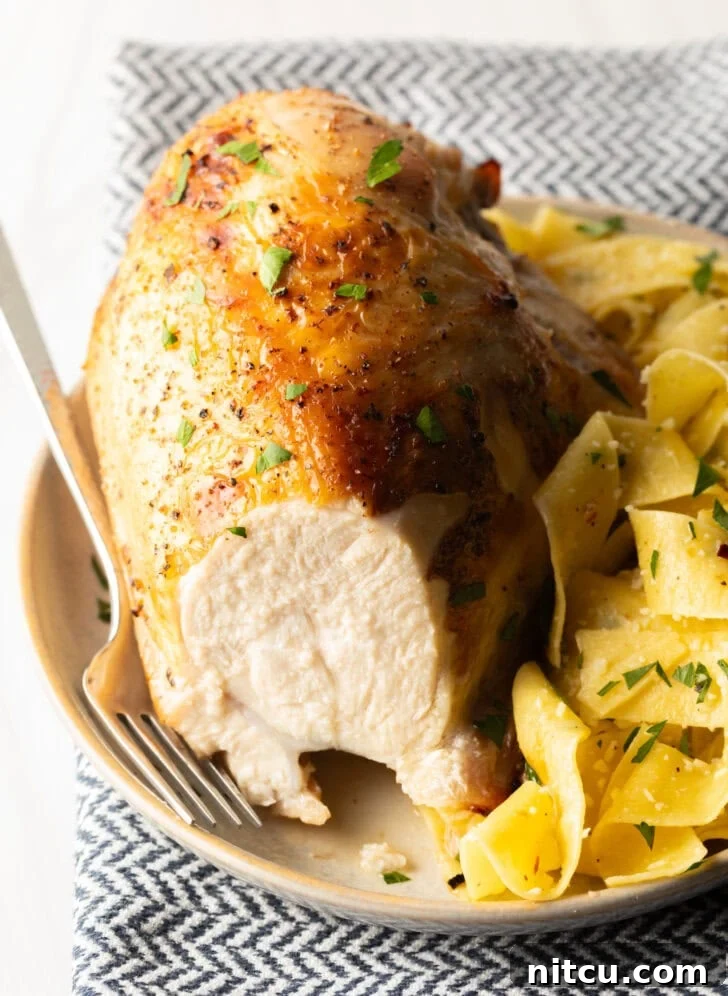 A delicious bourbon brined chicken breast on a white plate with a side of buttery noodles, with a forkful removed to highlight its moist and tender interior.