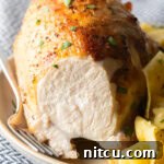 Bourbon brined chicken breast on a white plate with side of buttery noodles. A large bite has been removed from the chicken to show the moist interior.