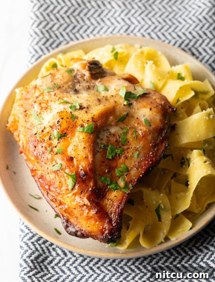 A perfectly cooked bourbon brined chicken breast on a white plate, served with a side of creamy, buttery noodles, ready to be enjoyed as a gourmet meal.