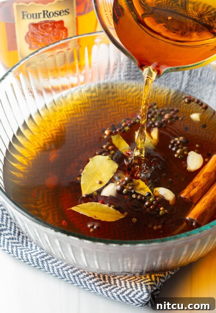 A smooth stream of rich amber bourbon being carefully added to the prepared brine mixture in a large glass bowl, contributing its signature depth and character.