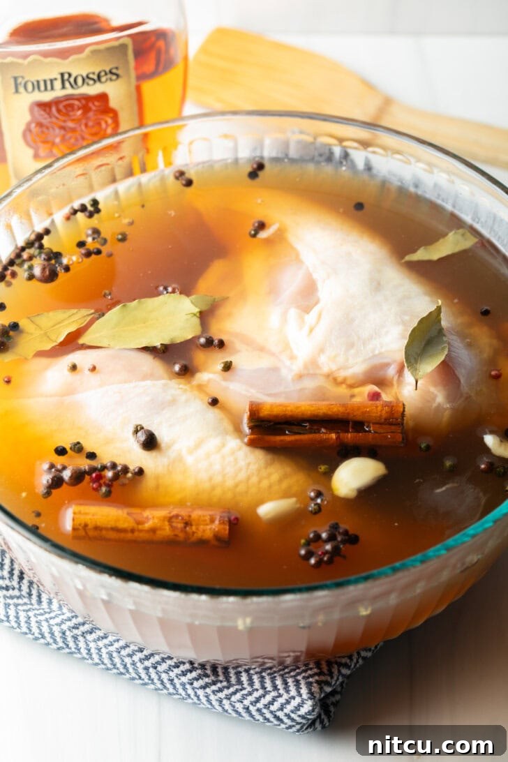 Two raw chicken breasts submerged in a clear bowl with the bourbon brine, visibly absorbing the flavorful liquid and preparing for optimal tenderness.