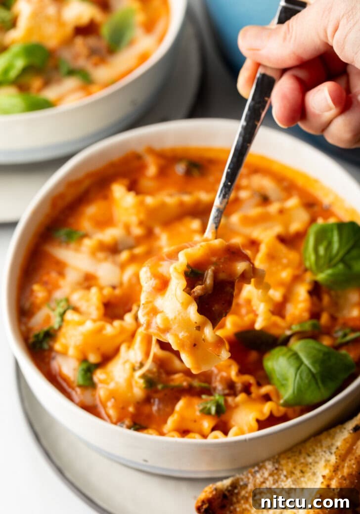 A spoon lifts a delicious bite of cheesy tomato soup with pasta and sausage, showcasing the delightful blend of textures and flavors.