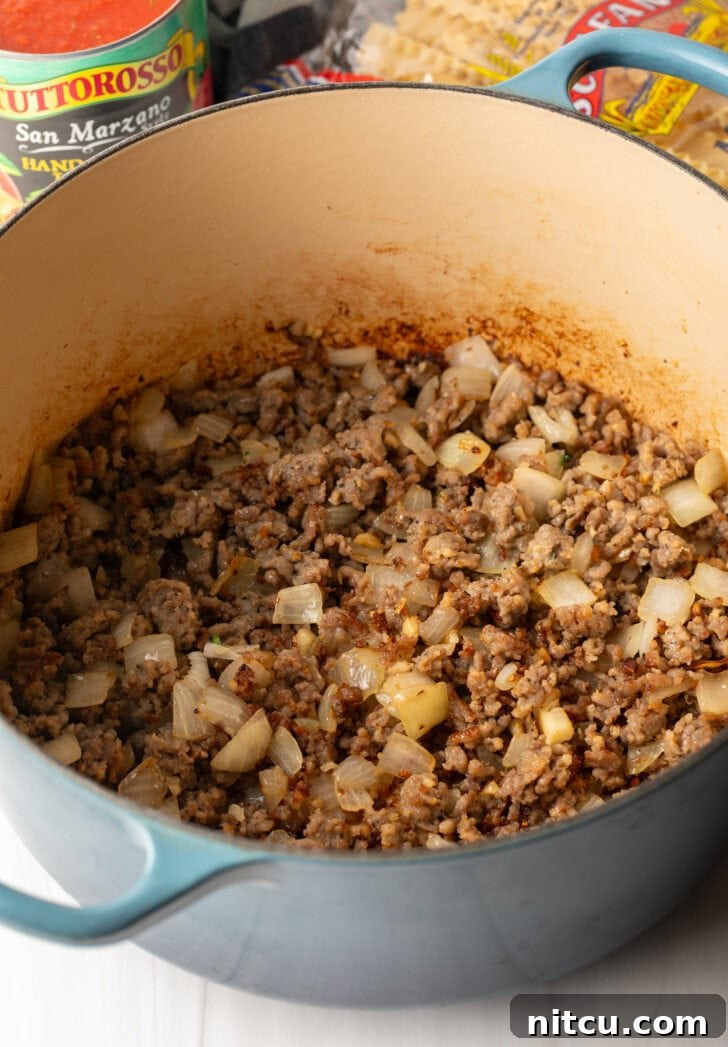 A large pot on the stove, containing perfectly browned ground sausage mixed with softened onions, preparing the flavor base for the soup.