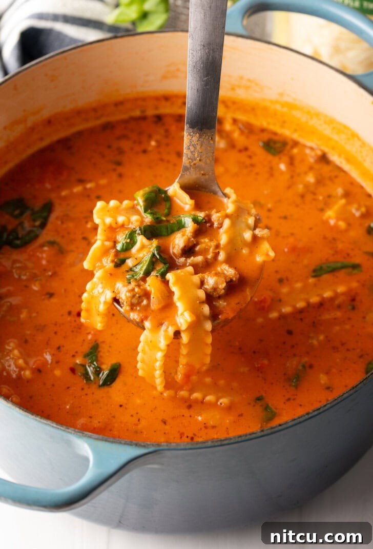 A ladle filled with savory lasagna soup, held above the pot, showcasing its inviting texture and readiness to be served.