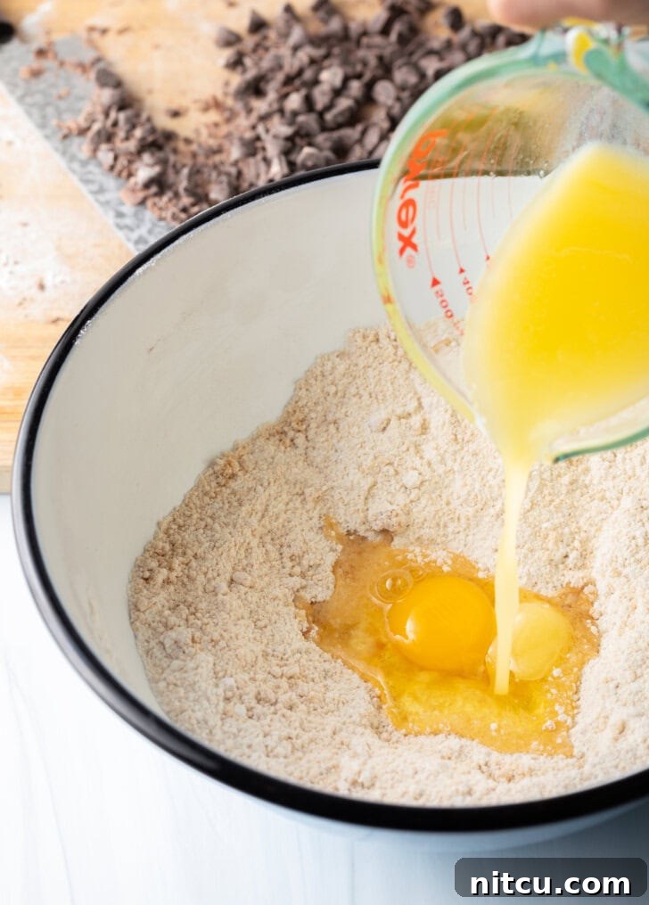 Adding melted butter to the white mixing bowl with dry ingredients