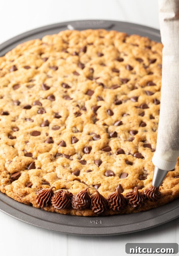 Piping chocolate frosting along the edge of the cookie cake.